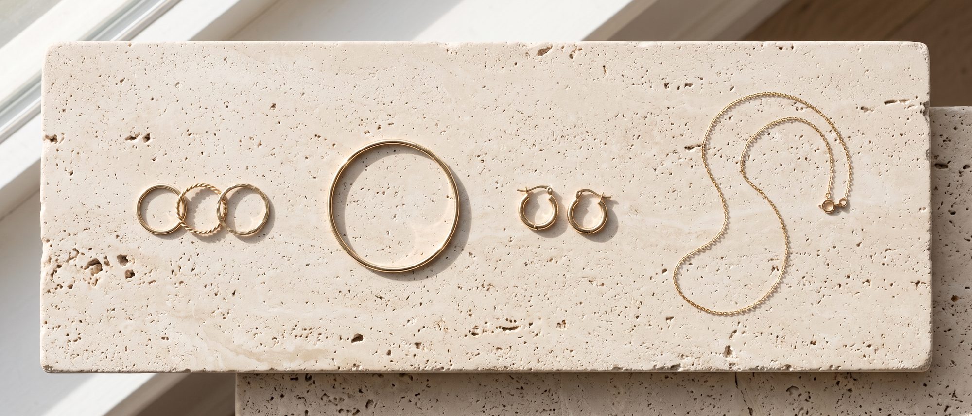 Overhead flat lay of fine gold jewellery on travertine